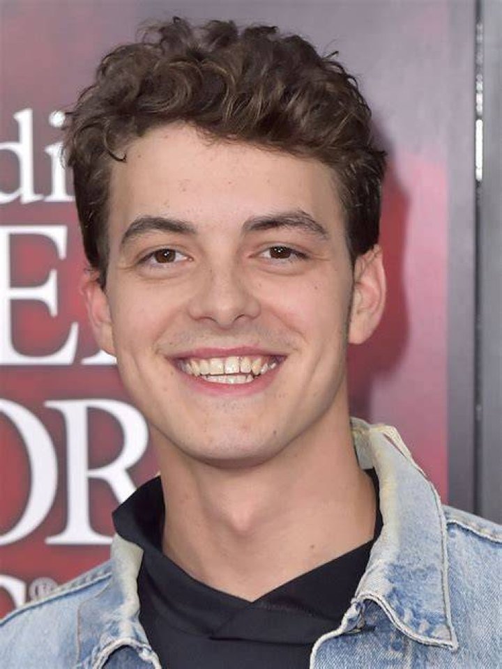 Israel Broussard posing by wearing white vest and black pant.